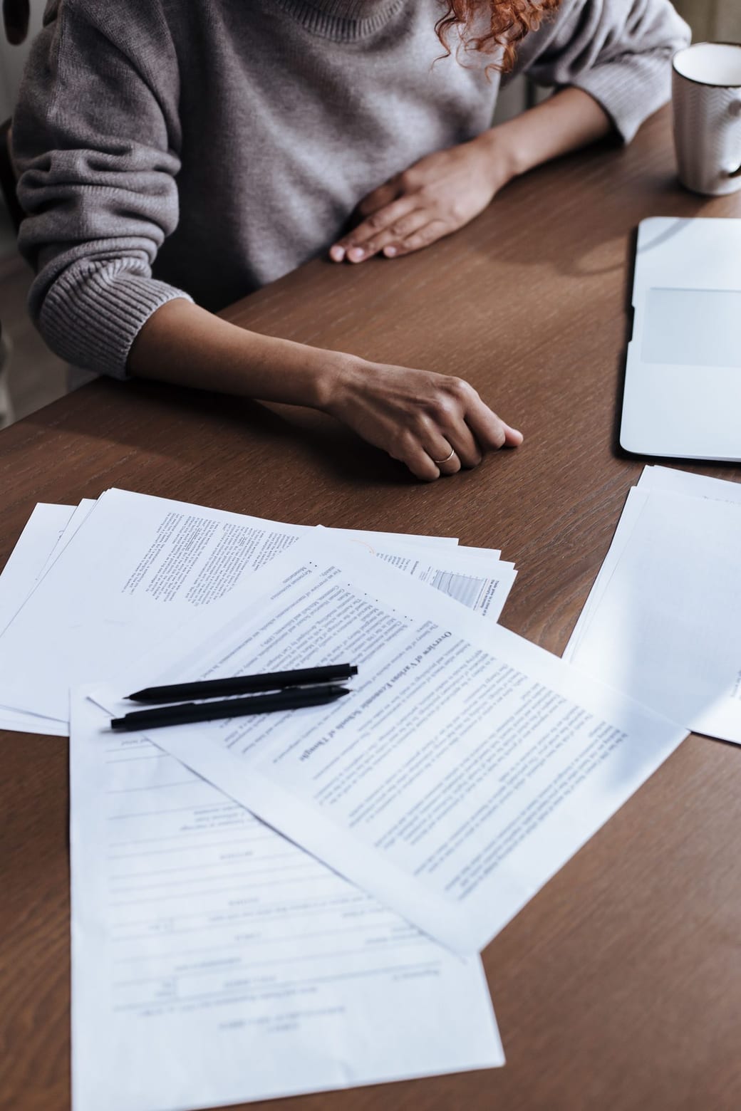 A hand resting on an open ring binder of tabbed, multi-page school records on a warm wooden table, a sticky note at the edge